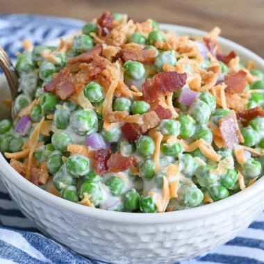 Classic pea salad with bacon served in a bowl, garnished with herbs.