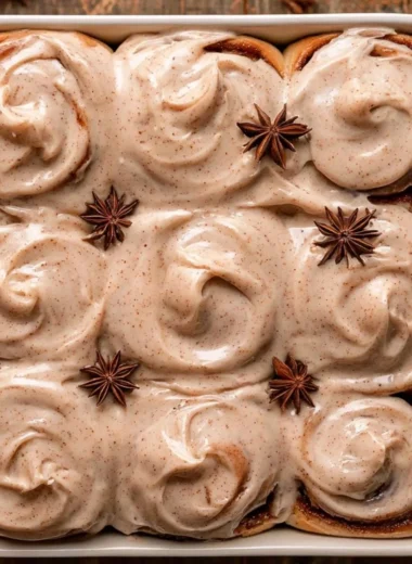 Gooey chai cinnamon rolls topped with icing and cinnamon on a rustic wooden table.