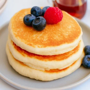 Stack of fluffy high protein pancakes topped with fresh berries and syrup