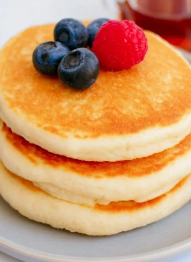 Stack of fluffy high protein pancakes topped with fresh berries and syrup