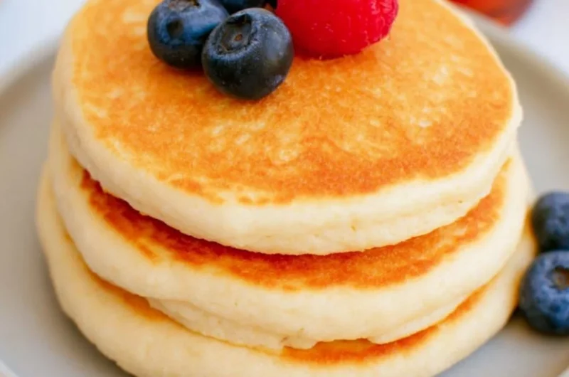 Stack of fluffy high protein pancakes topped with fresh berries and syrup